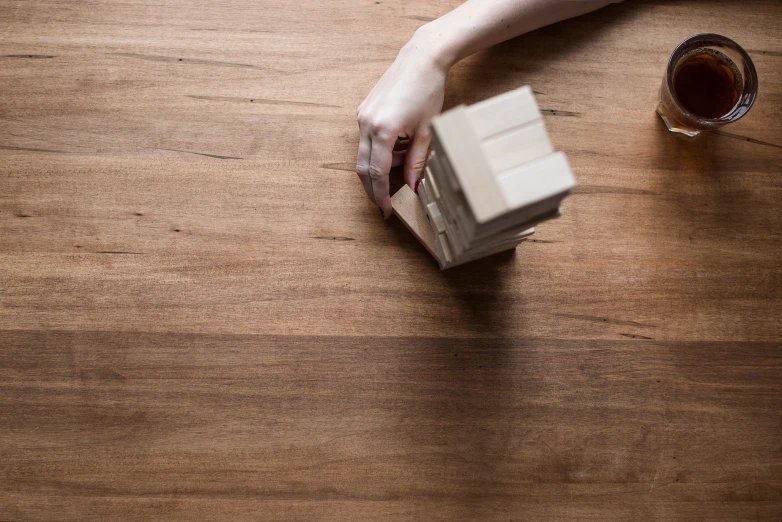 a hand grabbing a square piece of paper sitting on top of a wooden table