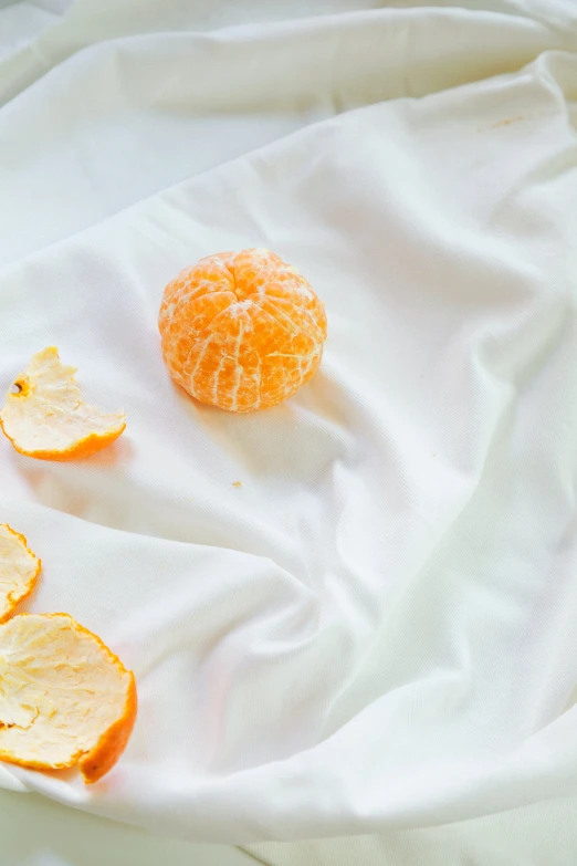 two peeled oranges are lying on white fabric