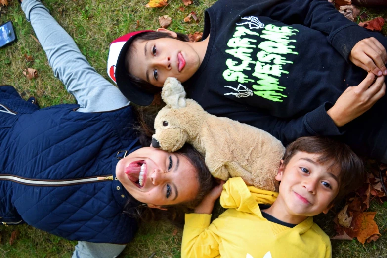 two children, one with a teddy bear lying on the ground