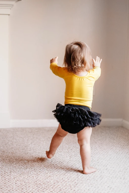a toddler wearing a yellow shirt and black skirt running around