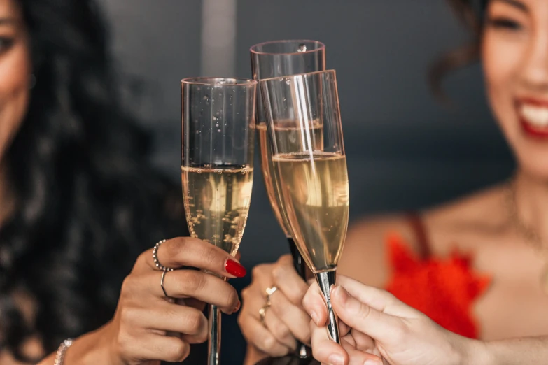 two women hold up champagne flutes with red fingernails