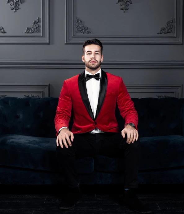 a man in a red tuxedo sits on a blue couch