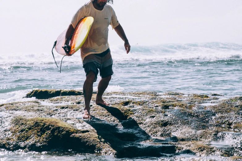 the man in shorts and t - shirt holds a surfboard while walking on the beach