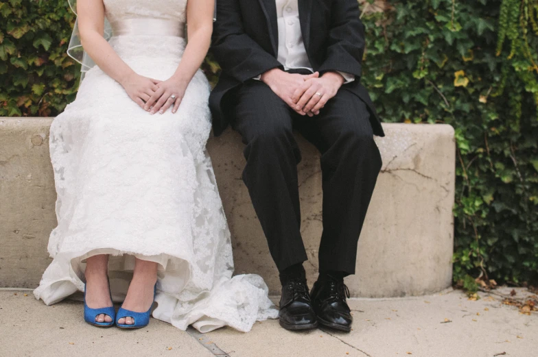 a man and woman sitting on a wall dressed in wedding attire