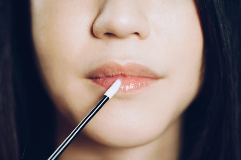 a close up of a woman holding an lip brush in front of her mouth