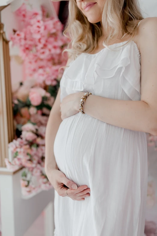 a pregnant woman in a white dress posing with a pink floral background