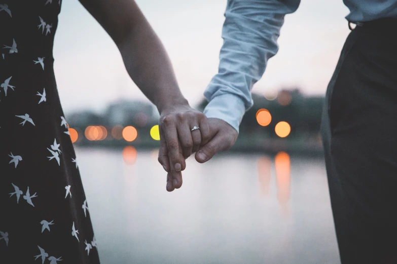 two people hold hands as they stand near water at dusk