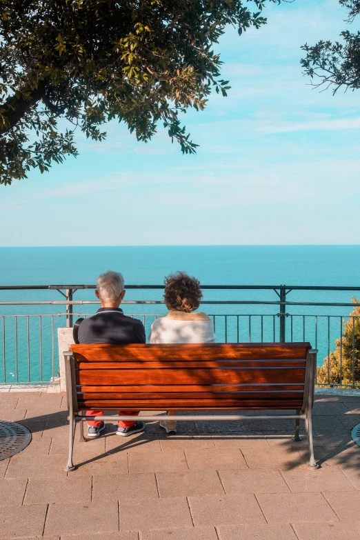 two people sitting on a bench looking out over the ocean