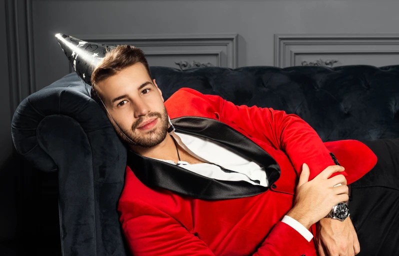 a man wearing a red jacket and hat is leaning on a black couch