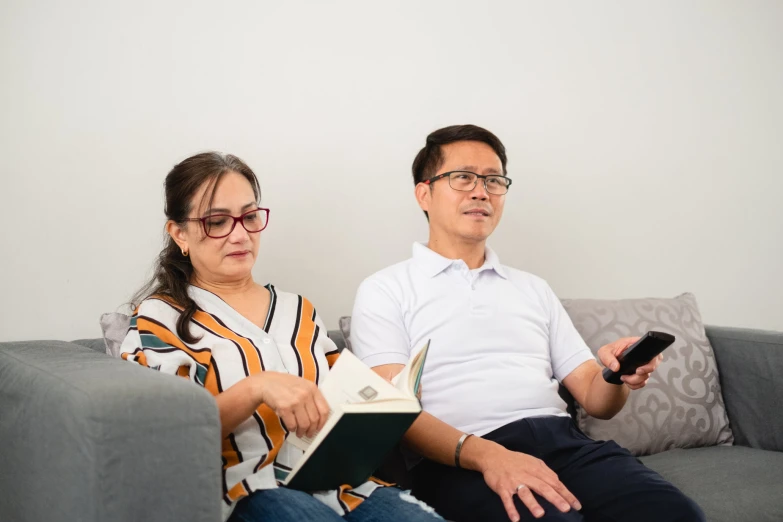 a man and woman sitting on a couch looking at a book