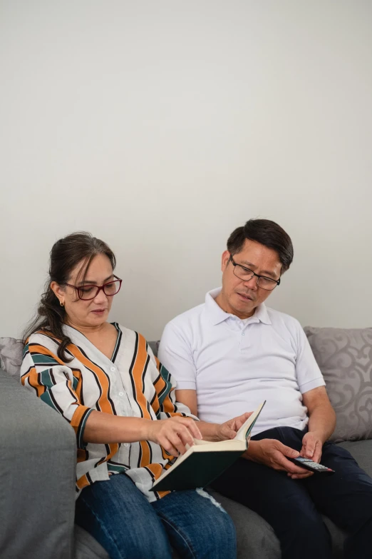 a man and woman sitting on a couch looking at a book
