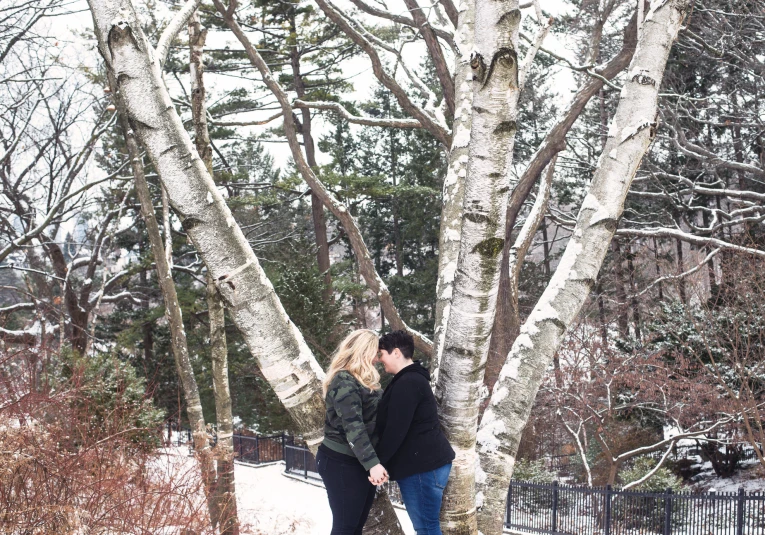 two people standing next to each other near a large tree