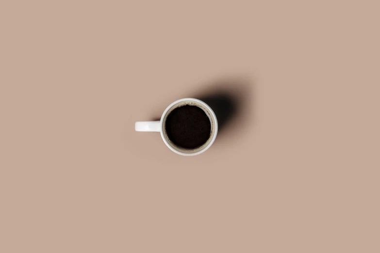 a white cup of coffee sits in a tan background