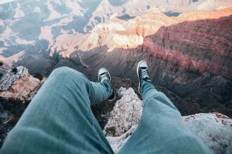 person wearing sneakers, sitting on top of the grand canyon