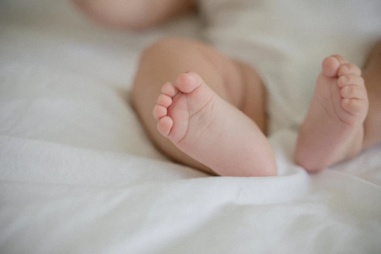 an infant's foot laying on the bed and under a blanket