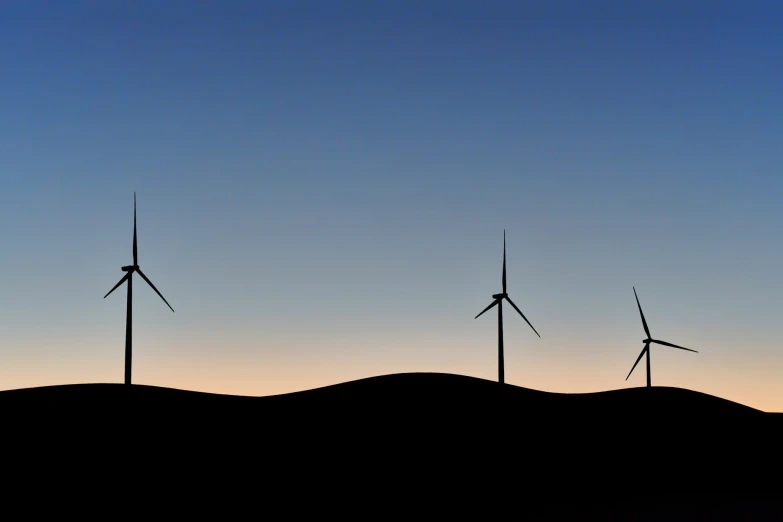 three wind mills are silhouetted against a sunset