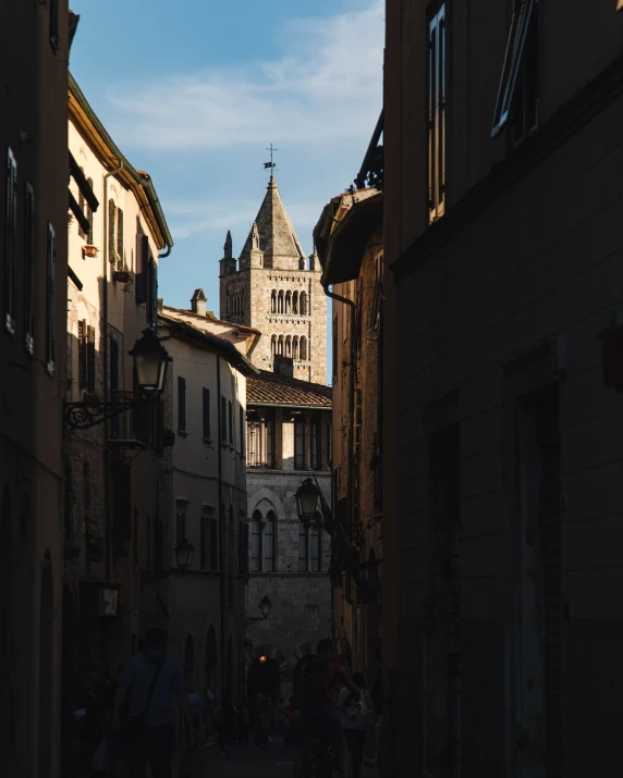 a clock tower is in the distance above people walking down a street