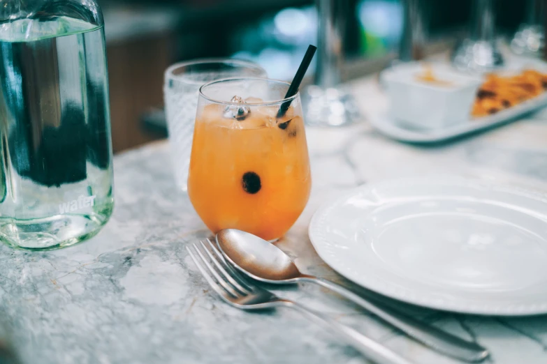 an orange beverage on a plate next to a glass with a straw