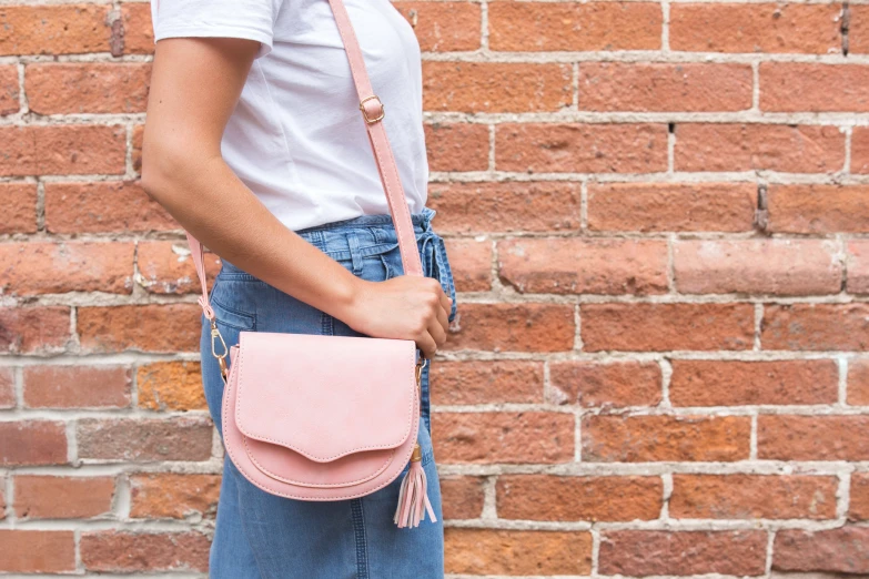 a  in jeans with a pink bag standing next to a brick wall