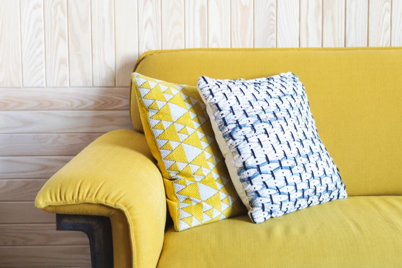 two decorative pillows sit on the back of a yellow sofa