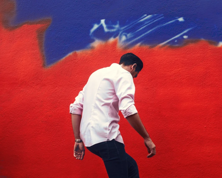 man walking against red wall with blue and white graffiti