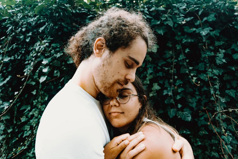 two people standing next to each other in front of bushes