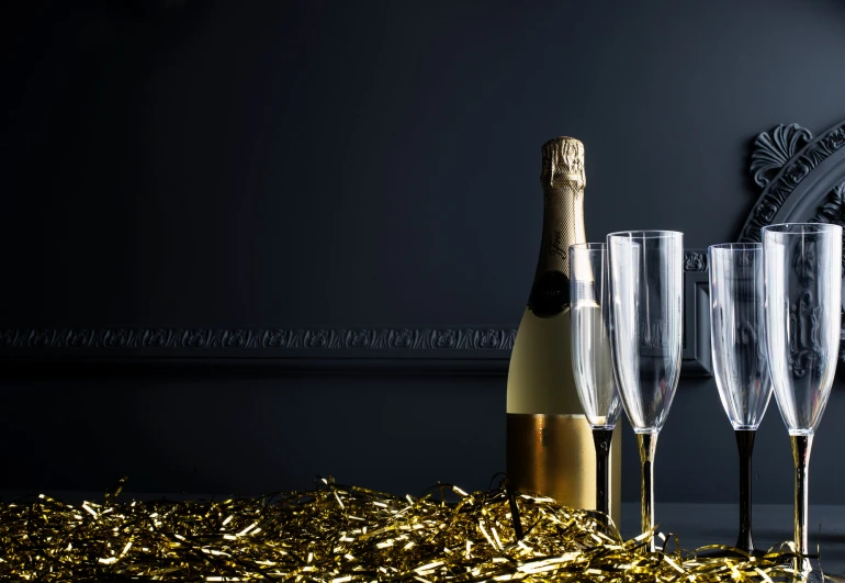 a bottle and four champagne flutes stand on gold foil