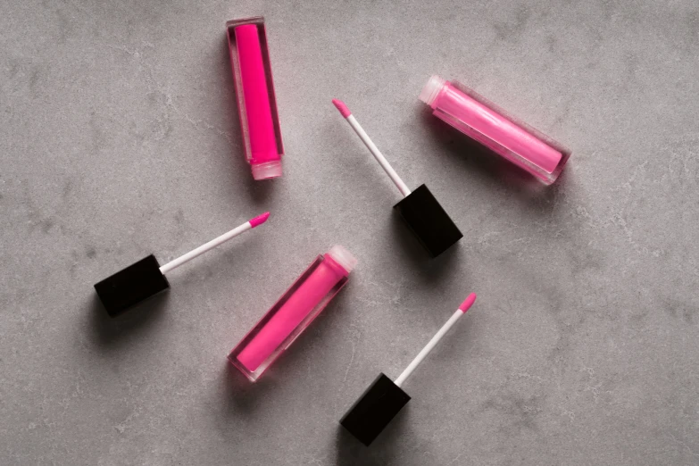 three pink and one black lipbrushes, two are on a gray surface