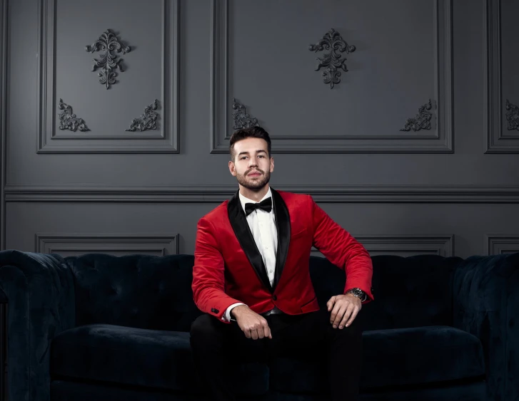 a young man in a red jacket, black pants and bow tie sitting on a couch