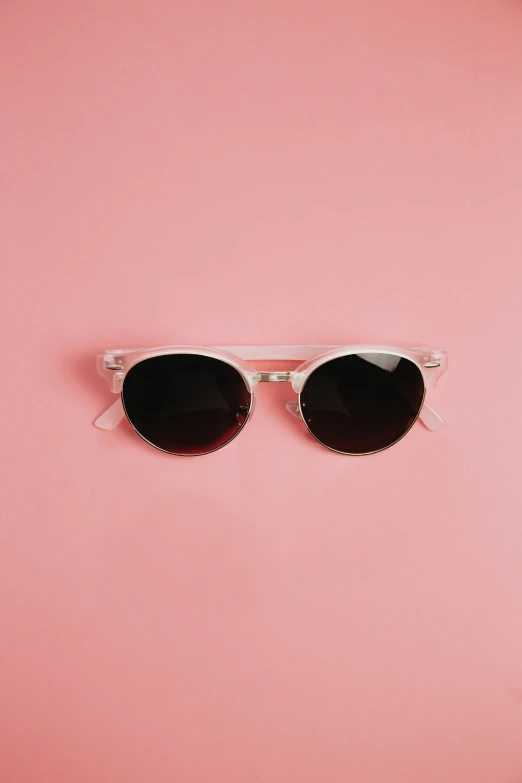 two sunglasses sit on a pink surface, the lens on top of the other pair