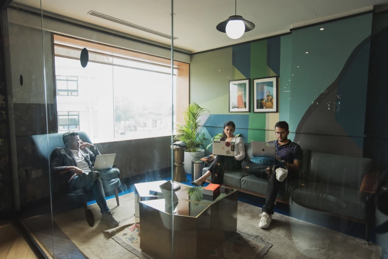 two men sitting in the sunlight on couches using laptop computers