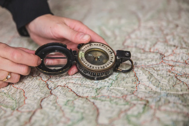 two hands holding a compass that is on top of a map