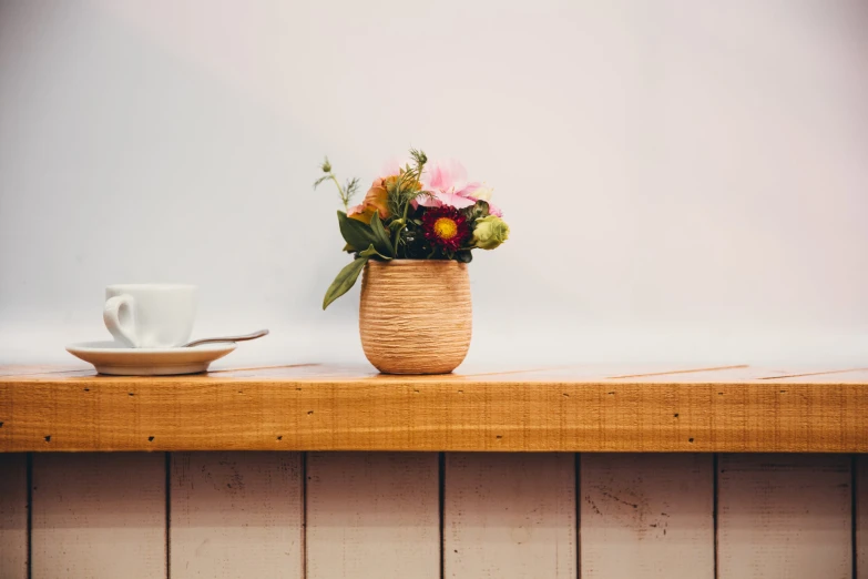 a white cup next to a wooden shelf with a vase on it