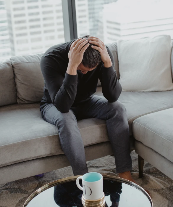 a man sits on the couch with his head in his hands