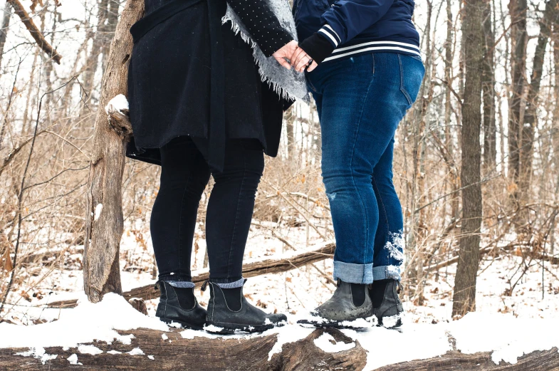 two women stand on top of logs in a snowy area