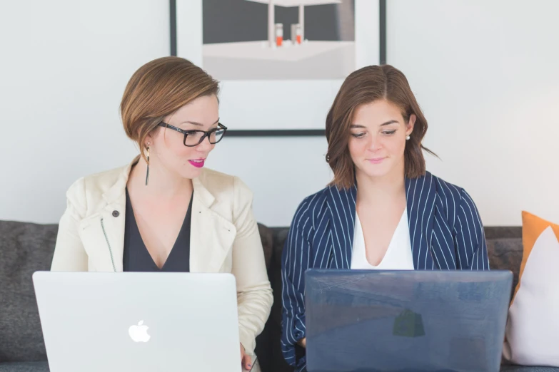 a girl sitting next to another girl on a couch using her laptop