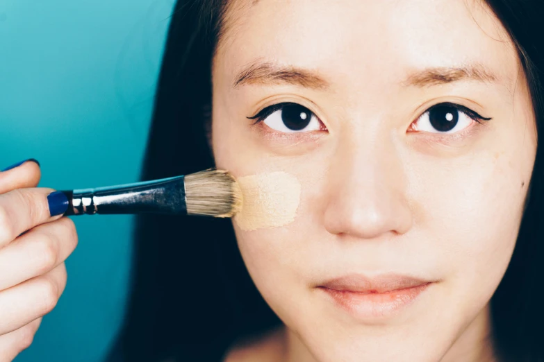 a girl with light brown hair brushes the light tan eye shadow on her face