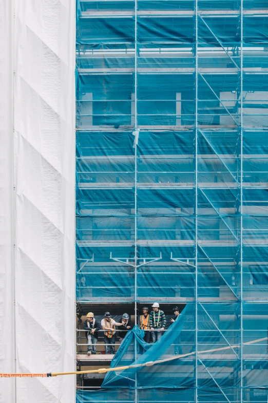 workers work on a scaffolding system in front of a blue building