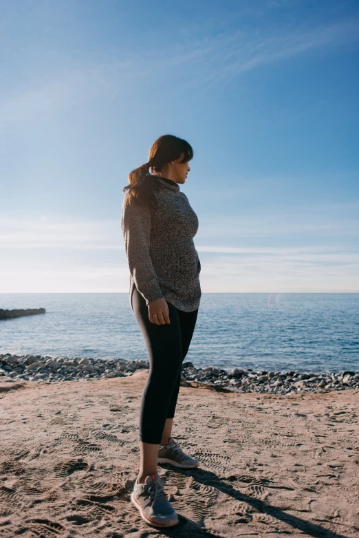 a woman in leggings and top standing on the beach by the water