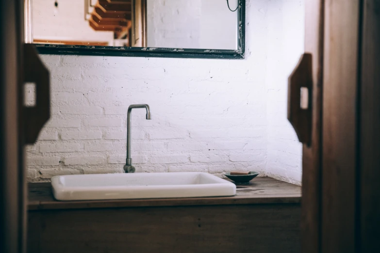 a white sink sitting next to a mirror on a brick wall