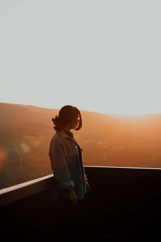 person standing on ledge of tower looking into sunset