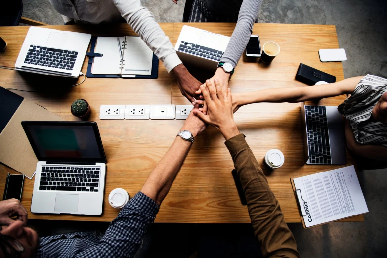 five people stacking their hands at the table with laptops