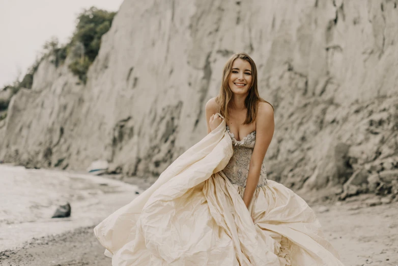 woman in wedding gown standing on beach next to large cliff