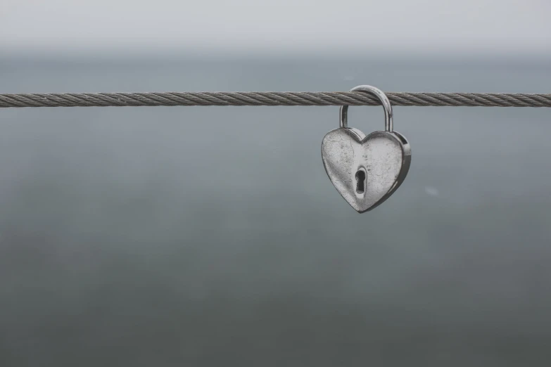 a heart - shaped lock is shown on a rope by the ocean