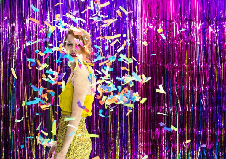 a young woman wearing yellow standing in front of confetti