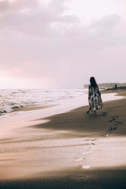 a girl in a long dress walks along the beach