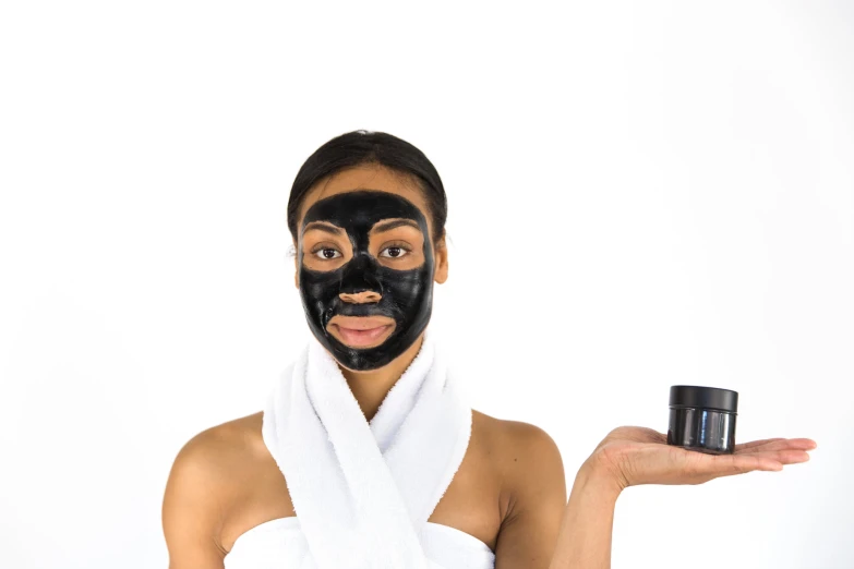 a woman wearing a black mask holding a cosmetic bottle in her hand