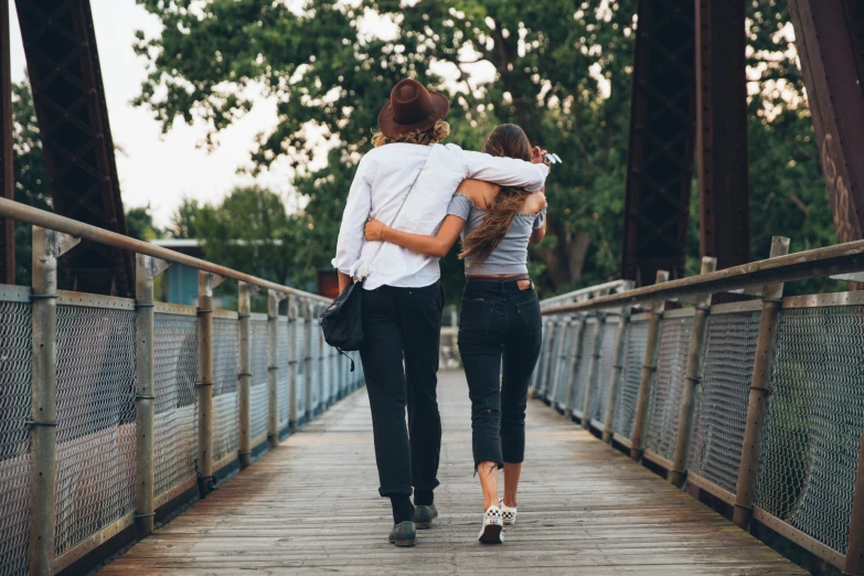 two women walking across a bridge in the woods