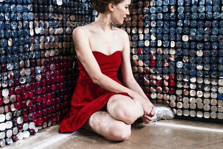 a woman sitting on the floor in front of a wall full of bottle caps