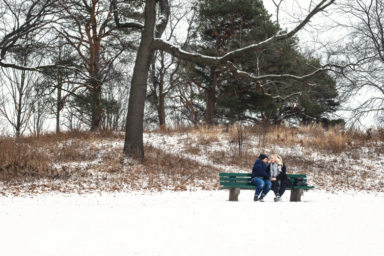 two people sitting on a park bench in a field